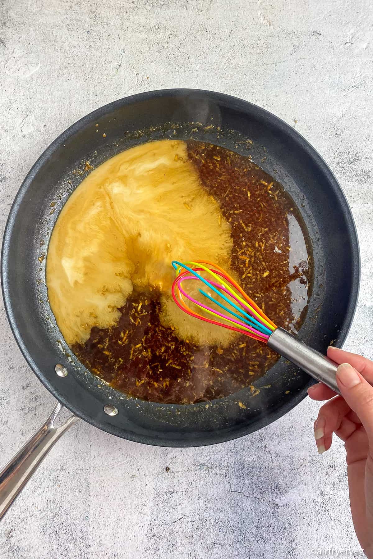 Hand mixing teriyaki sauce in a skillet.