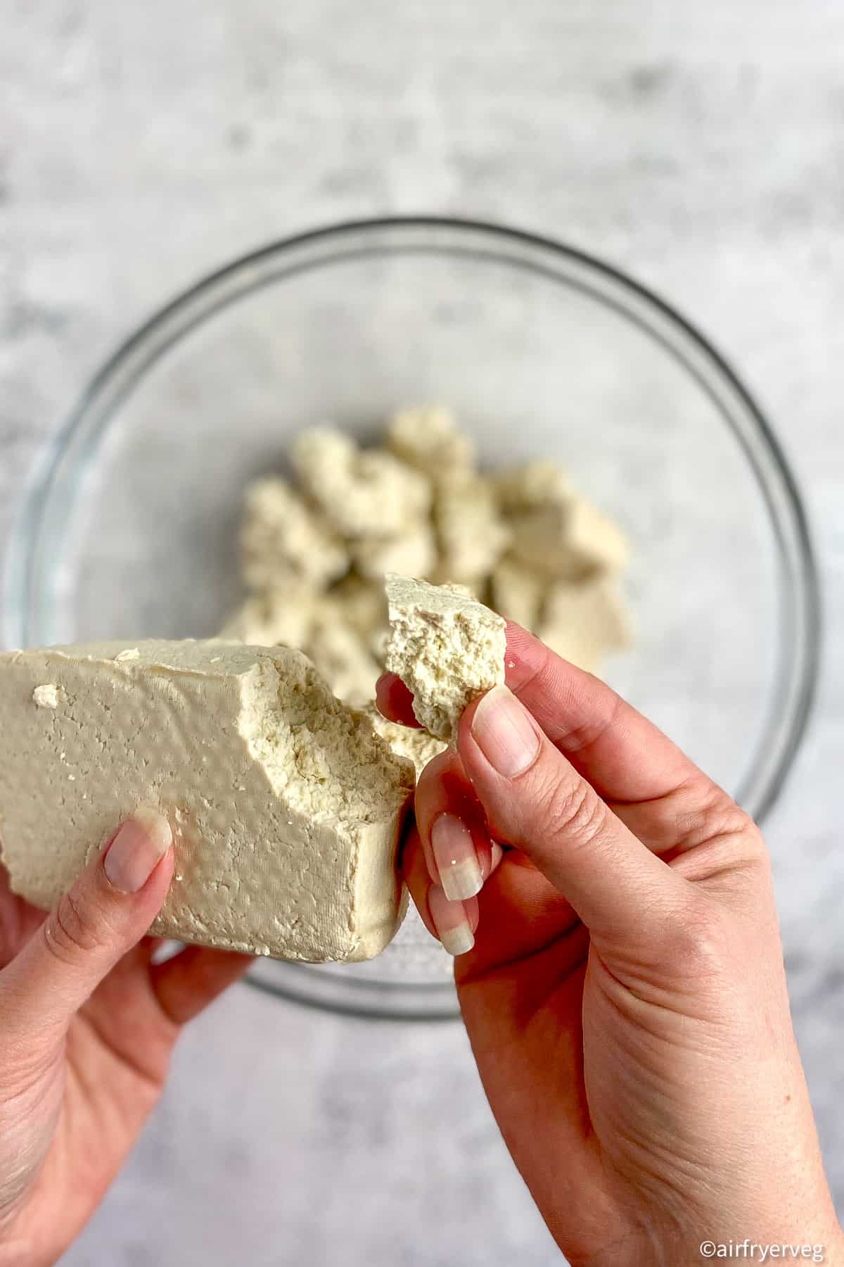 Hands breaking tofu into chunks.