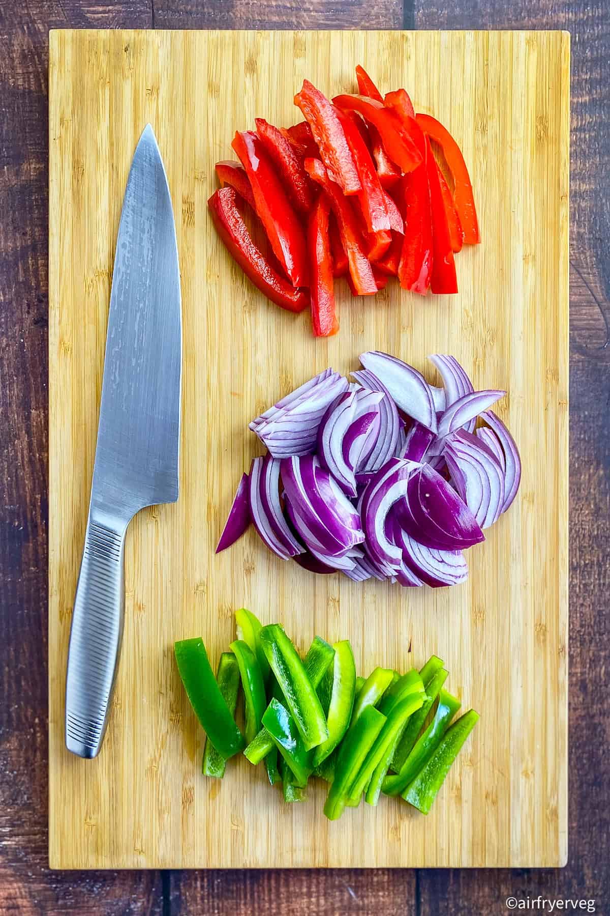 Bell peppers and onions cut into strips on a cutting board.